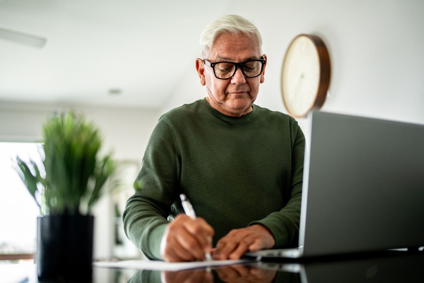 An elderly man writing in front of his computer 